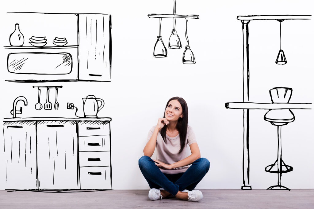 Dreaming about new kitchen. Cheerful young woman smiling while sitting on the floor against white background with drawn kitchen