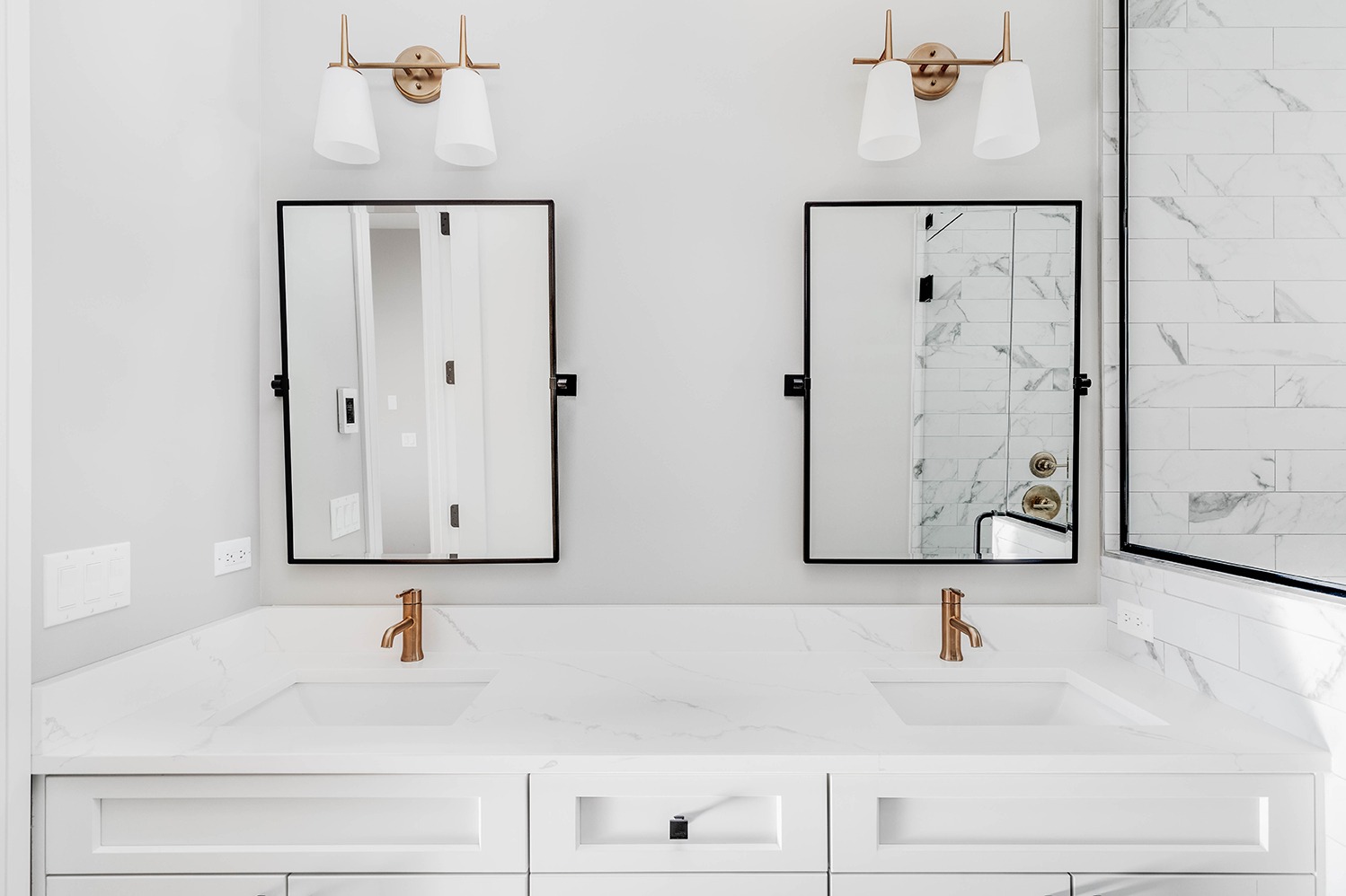 An all white bathroom with gold hardware and faucets in a downtown condo with the lights off.