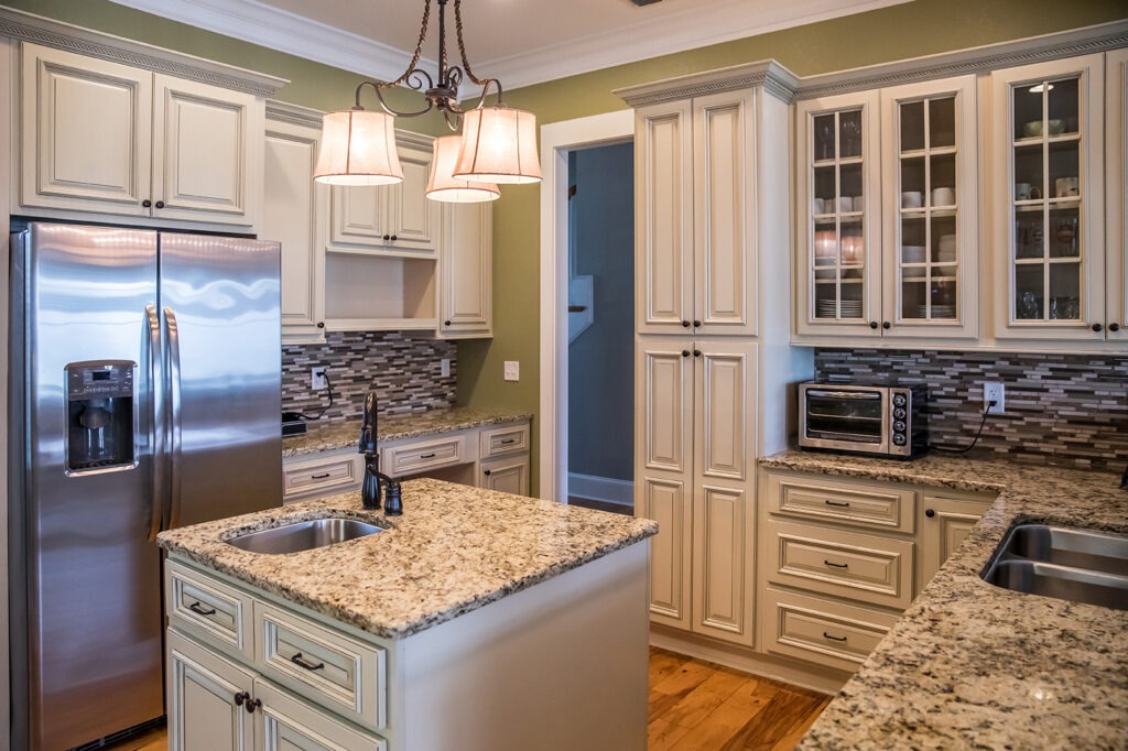 A square shaped green kitchen with cream colored cabinets in a new construction home with granite countertops and lots of cabinets and storage space with an island a sink