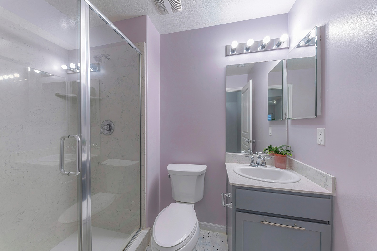 Small traditional bathroom interior with toilet, vanity sink, and shower stall. Bathroom interior with shower with glass wall and door near the toilet bowl beside the sink with mirror on the left.