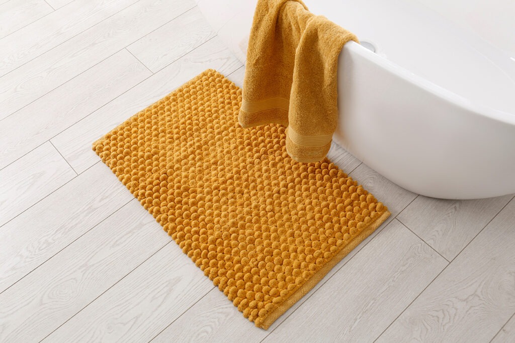 Soft orange bath mat on floor in bathroom