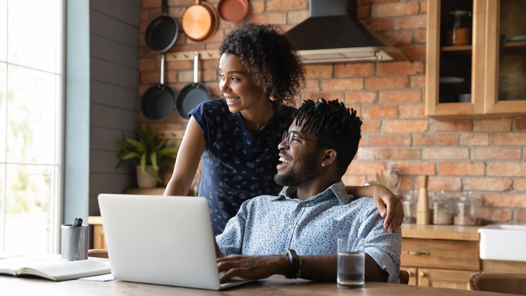 Close up happy dreamy African American couple distracted from laptop, visualizing good future, planning, looking to aside, smiling wife and husband spending leisure time in kitchen together
